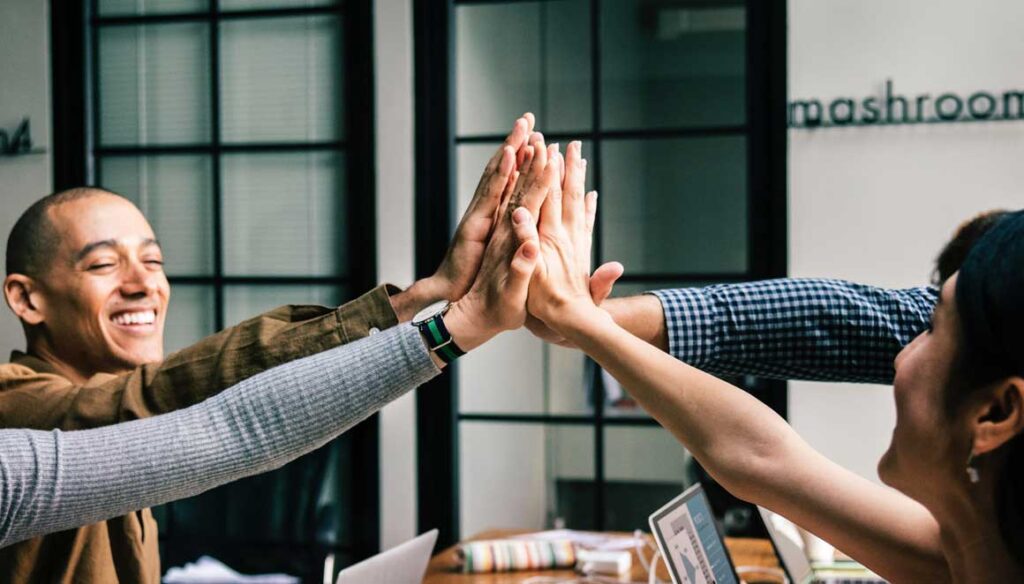 A group of cheerful coworkers giving a high-five in a modern office, celebrating teamwork and success